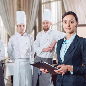 Restaurant manager standing confidently with a team of chefs in a fine dining restaurant setting, symbolizing leadership in hospitality management.