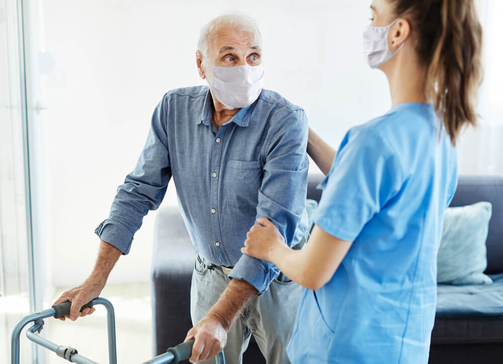 Nurse ensures patient safety while assisting an elderly man with a walker