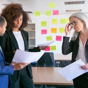 Three business professionals engaged in a strategic planning meeting, discussing marketing analysis with colorful sticky notes on the wall behind them.