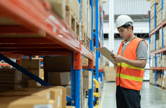 Warehouse worker in safety vest and helmet conducting inventory in supply chain management